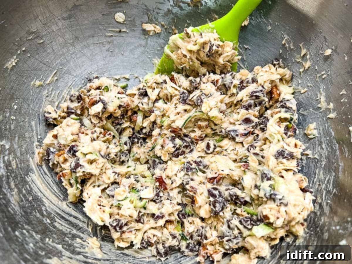 Oats, nuts, and chocolate chips being folded into zucchini cookie dough with a spatula.