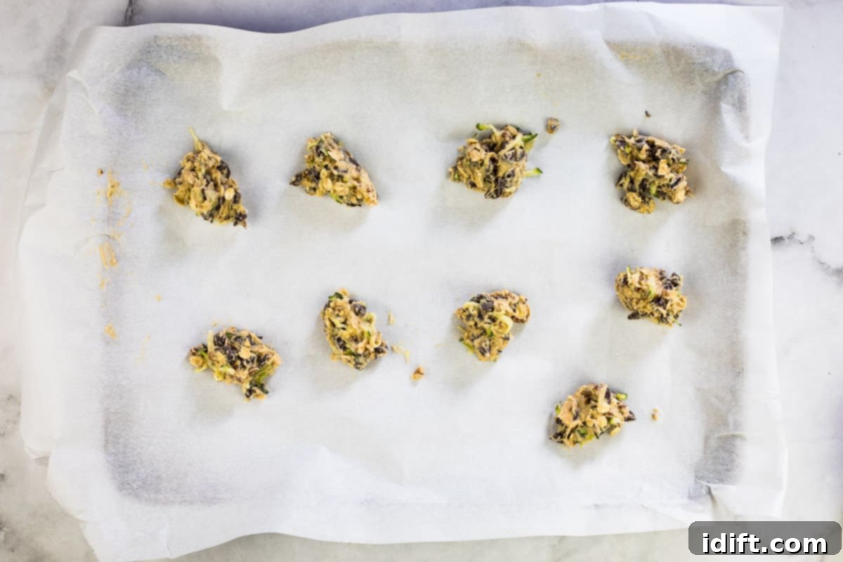 Portioned zucchini cookie dough on a parchment paper-lined baking sheet, ready for the oven.