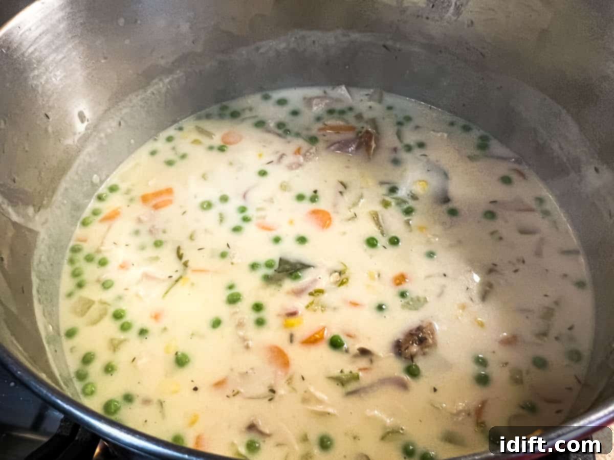 Adding cooked turkey, peas, and corn to the simmering soup.