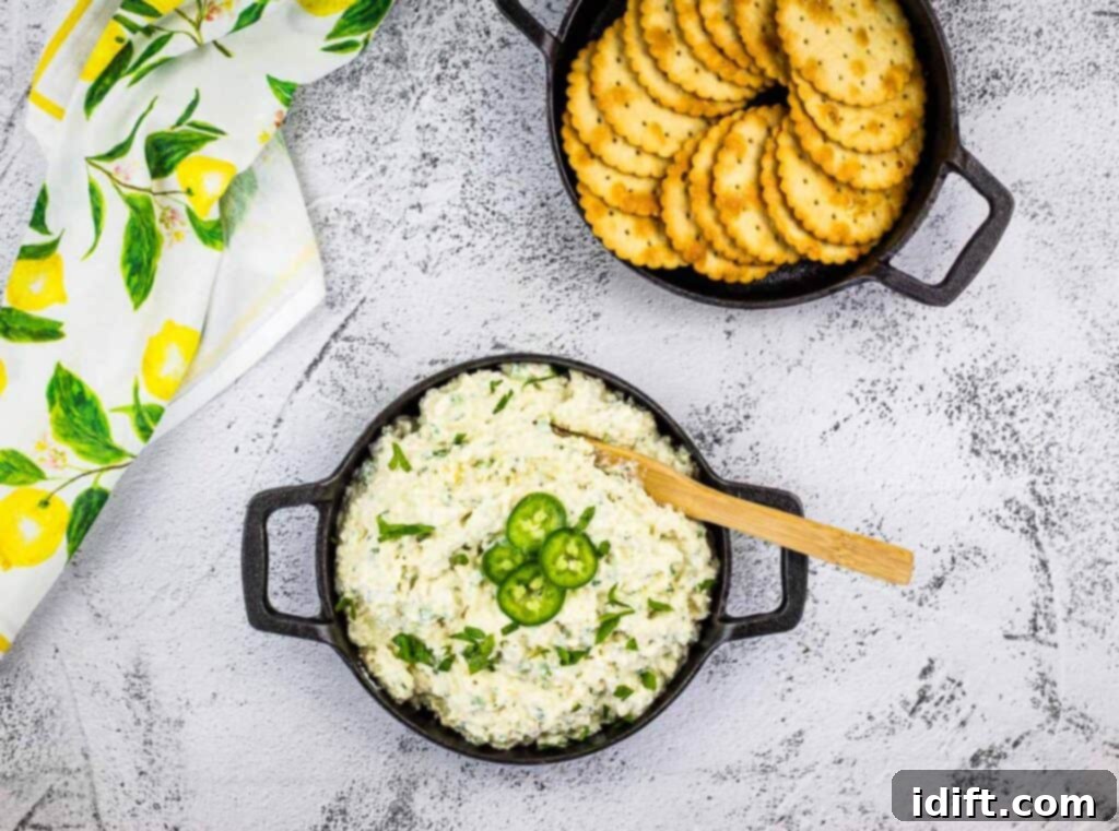 Creamy Jalapeno Artichoke Dream 9 A top-down shot of a black bowl filled with creamy Artichoke Jalapeno Dip, garnished with fresh parsley, surrounded by an array of crunchy crackers.