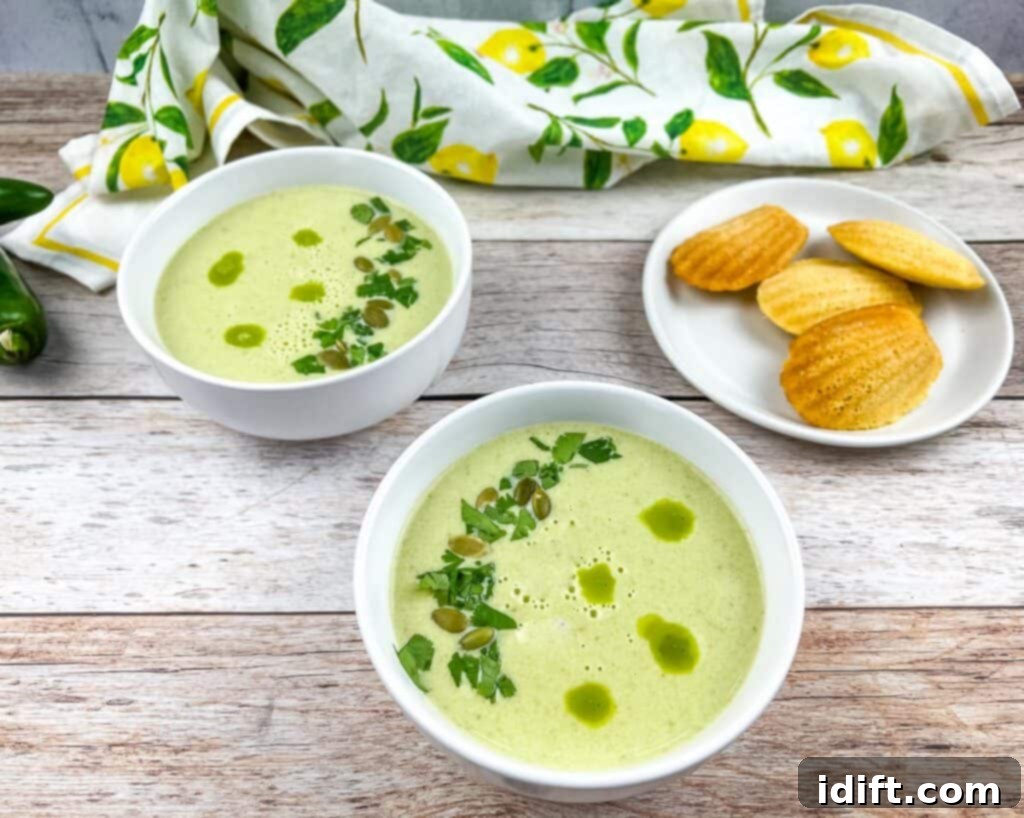 Jalapeno Velvet Warmth 3 Two bowls of Cream of Jalapeno Soup, artfully arranged, with cornbread madeleines visible in the background, creating an inviting culinary scene.