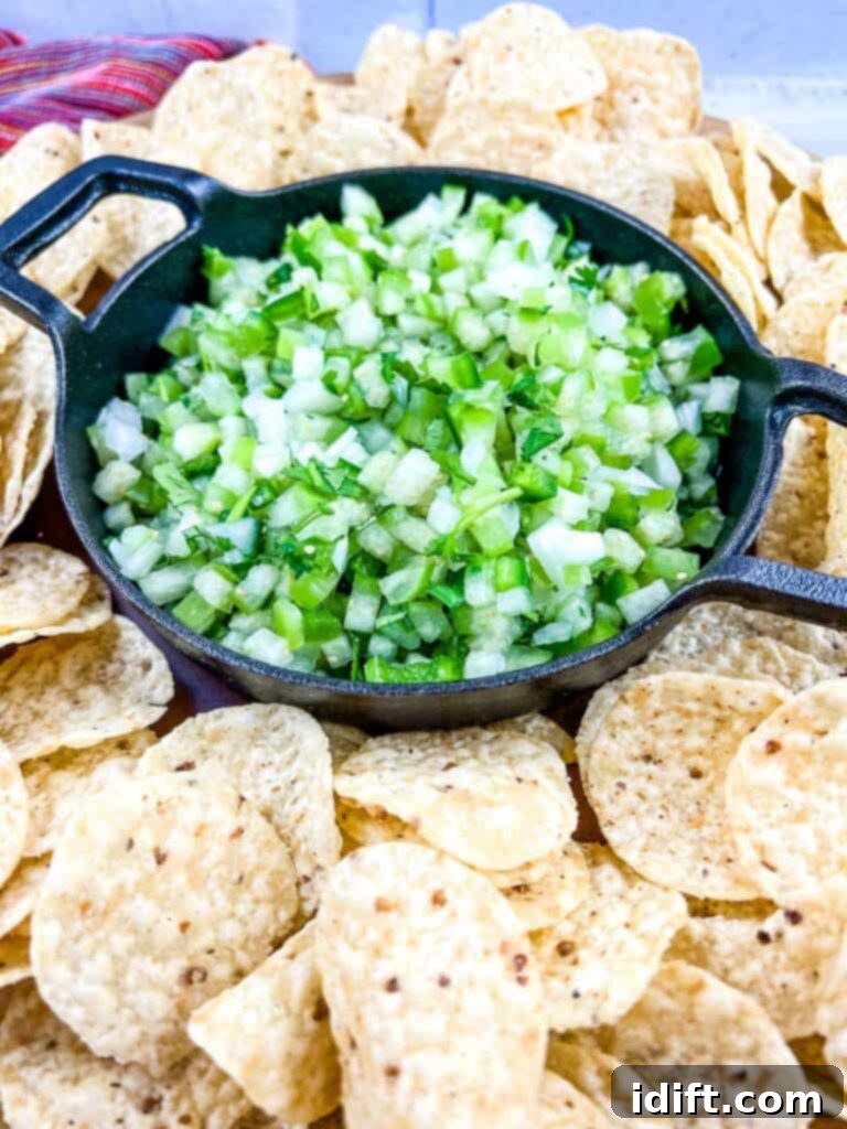 Tomatillo Pico de Gallo in a black dish with tortilla chips around it.