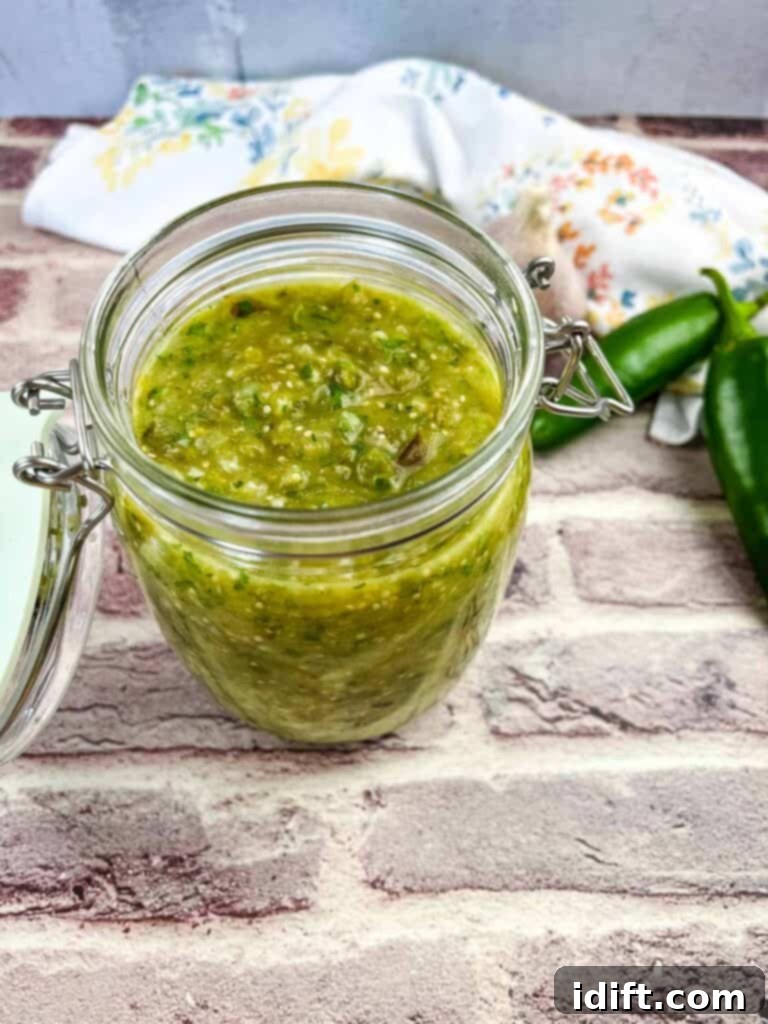 Creamy tomatillo sauce in a jar with jalapenos in the background.