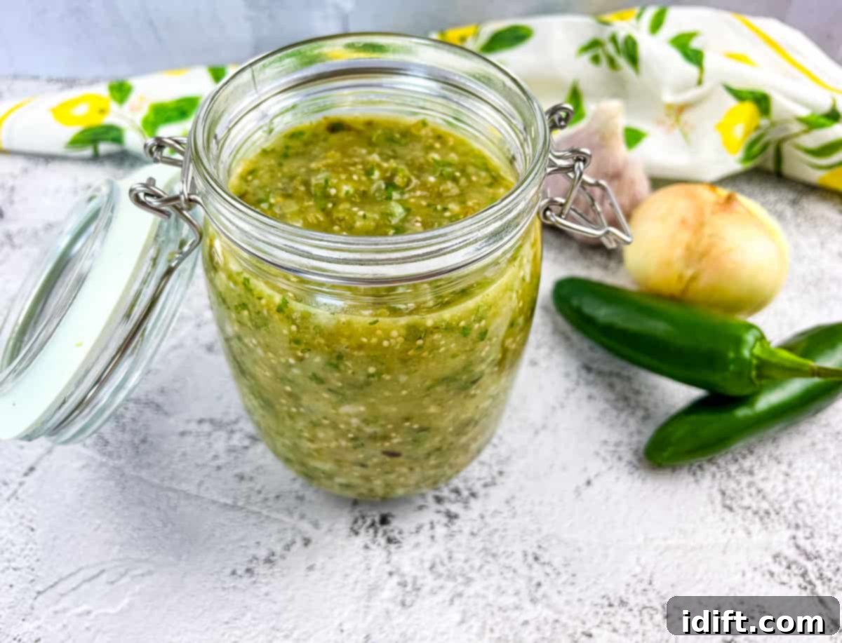 Tomatillo sauce in a glass jar with veggies in the background.