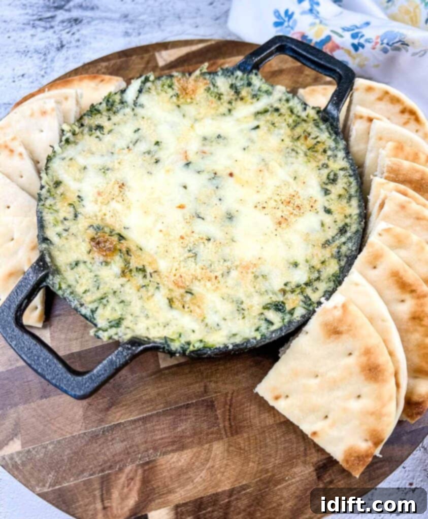 Spinach and Brie Dip in a cast-iron dish with pita chips around it.