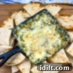 Spinach and Brie Dip in a cast-iron dish with pita chips around it.