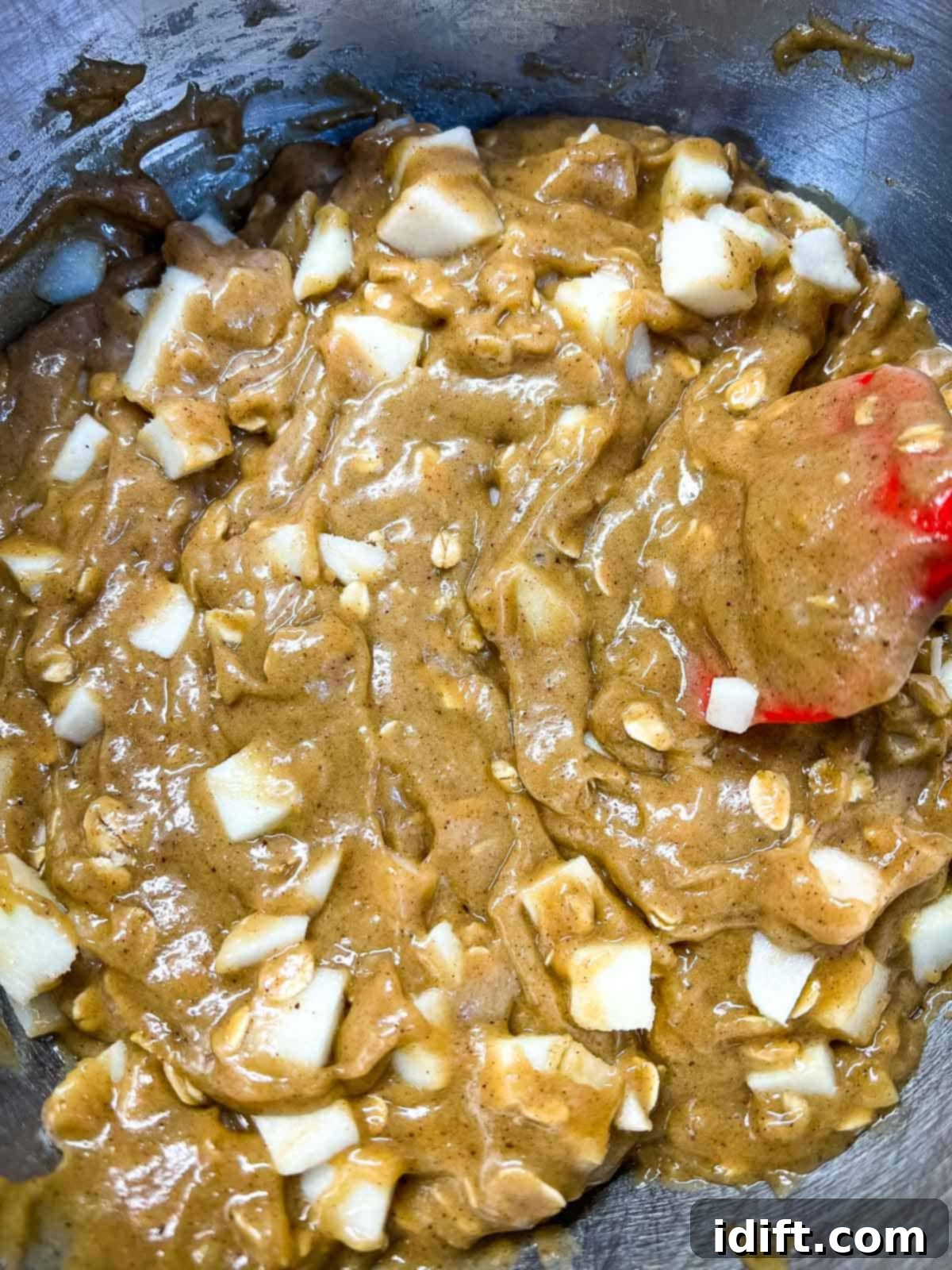 Diced apples and oats being folded into the blondie batter with a spatula.