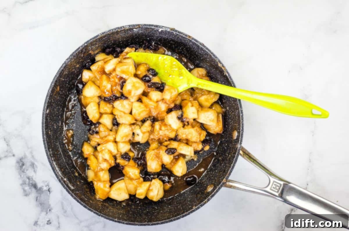 The apple filling, now thickened and vibrant with cranberries, simmering gently in a skillet, ready to be cooled.