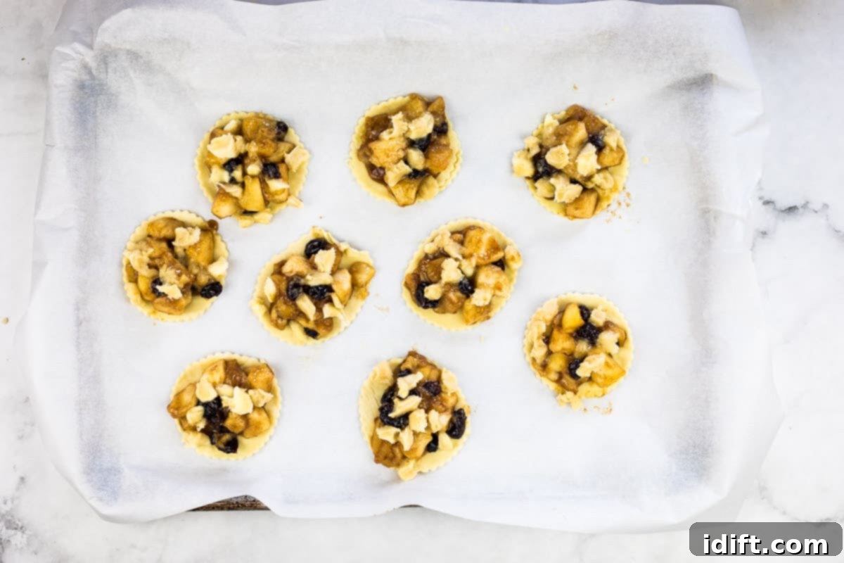 Individual apple-cranberry puff pastry tarts, generously topped with the fruit mixture and crumble, arranged on a baking sheet, ready for the oven.