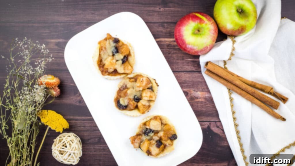 Freshly baked apple-cranberry puff pastry tarts arranged neatly on a pristine white plate, showcasing their golden crusts and vibrant fruit filling.