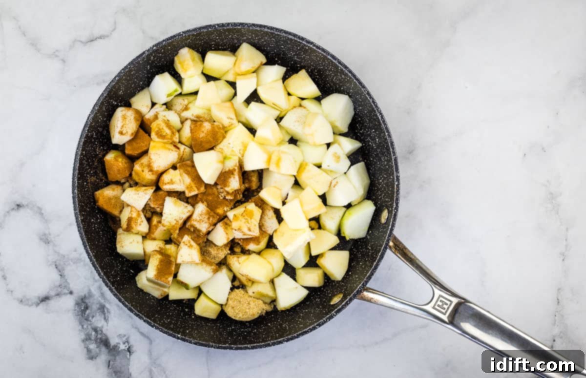 Apples, butter, and brown sugar simmering in a skillet over medium heat, releasing their juices and softening.