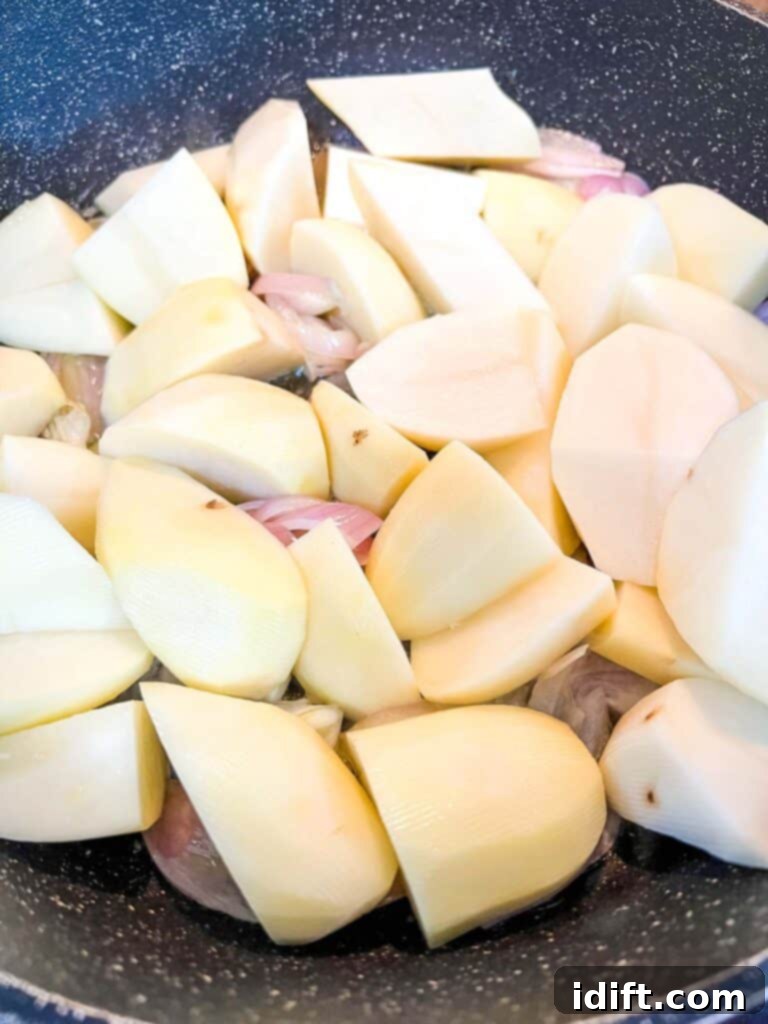 Rustic Rosemary Garlic Potato Braise 7 Chopped potatoes being added to a skillet with sautéed shallots, ready to be tossed and browned.