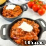 A closeup shot of Smoked Brisket Chili in 2 black bowls with bread and tomatoes in the background.