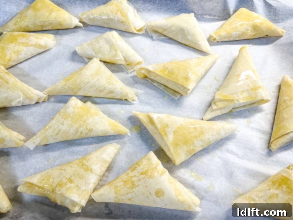 Unbaked Crab Spanakopita triangles on a baking sheet.