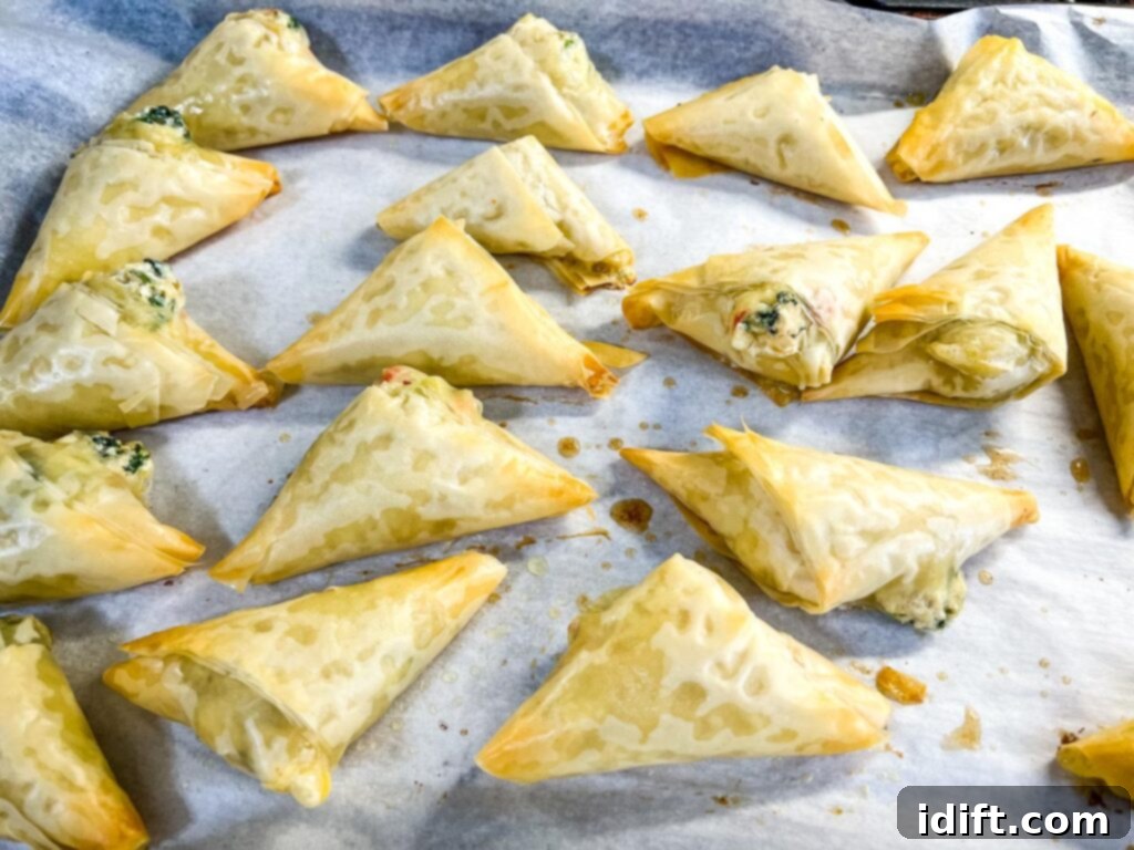 Golden brown baked Crab Spanakopita triangles on a baking sheet.