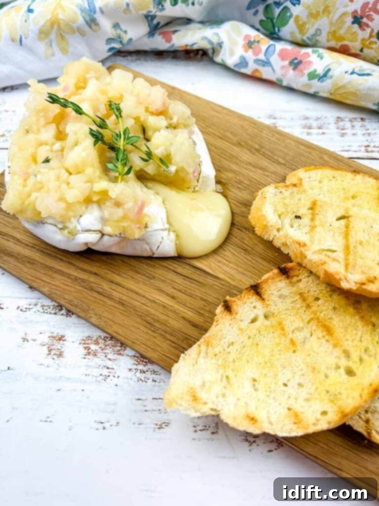 Beautifully baked brie with a generous topping of homemade apple ginger chutney, served on a rustic wooden board alongside grilled bread slices.
