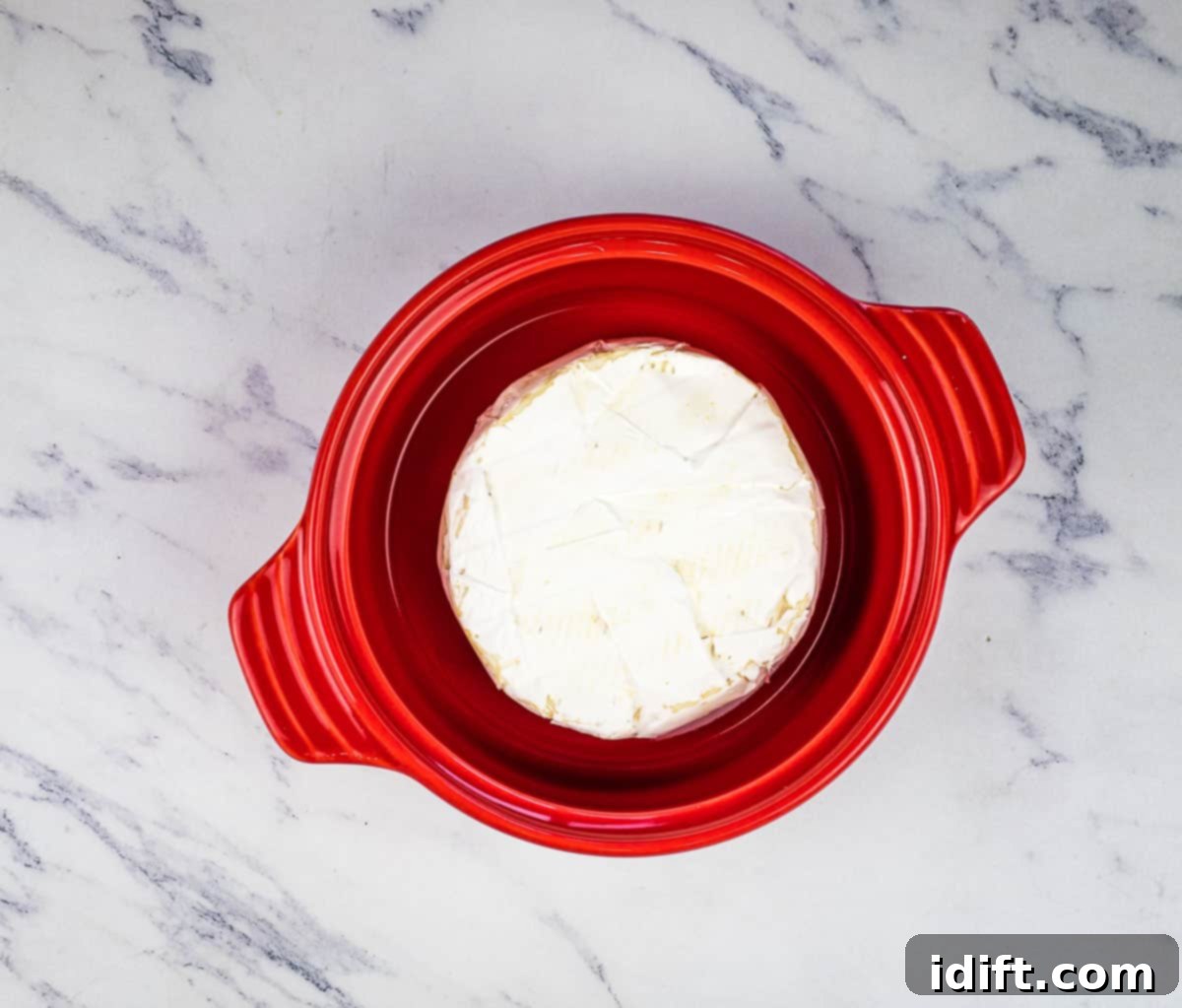 A pristine wheel of brie cheese placed inside a charming ceramic brie baker, prepared for oven baking.