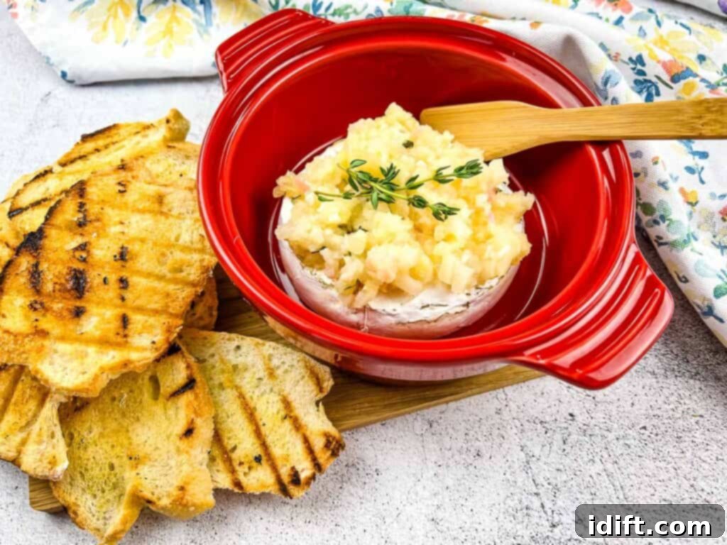 Baked brie elegantly presented in a vibrant red ceramic brie baker, topped with golden apple ginger chutney.