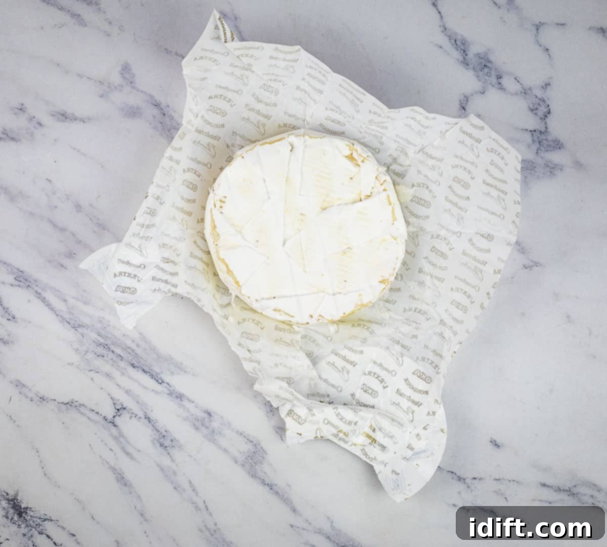 A fresh wheel of brie cheese, carefully unwrapped from its packaging, ready for the baking process.