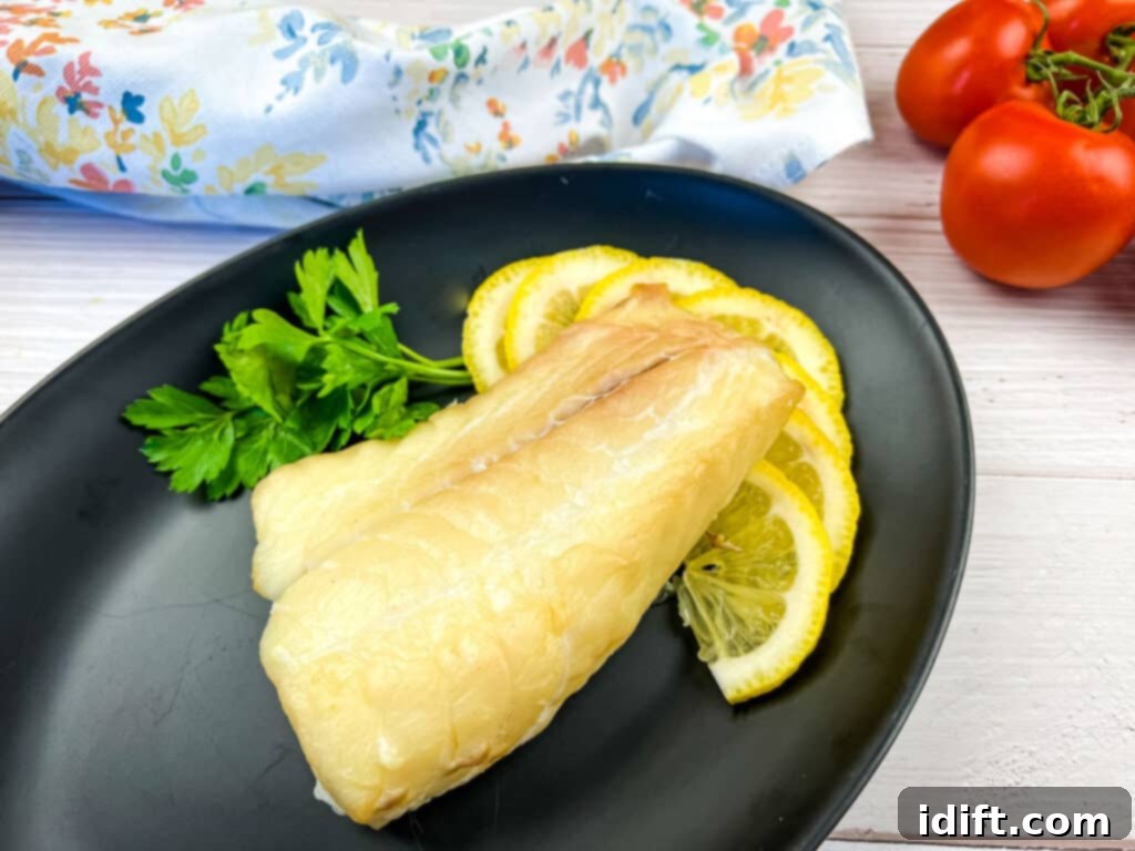 Smoked cod filet on a black plate with lemon.