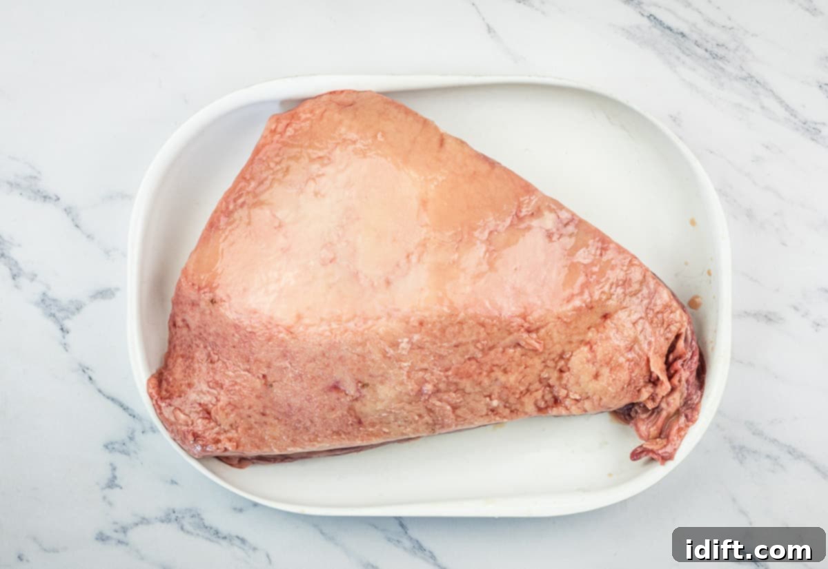 Perfectly Smoked Picanha 6 Raw picanha roast on a white plate, showing its fat cap and lean muscle.