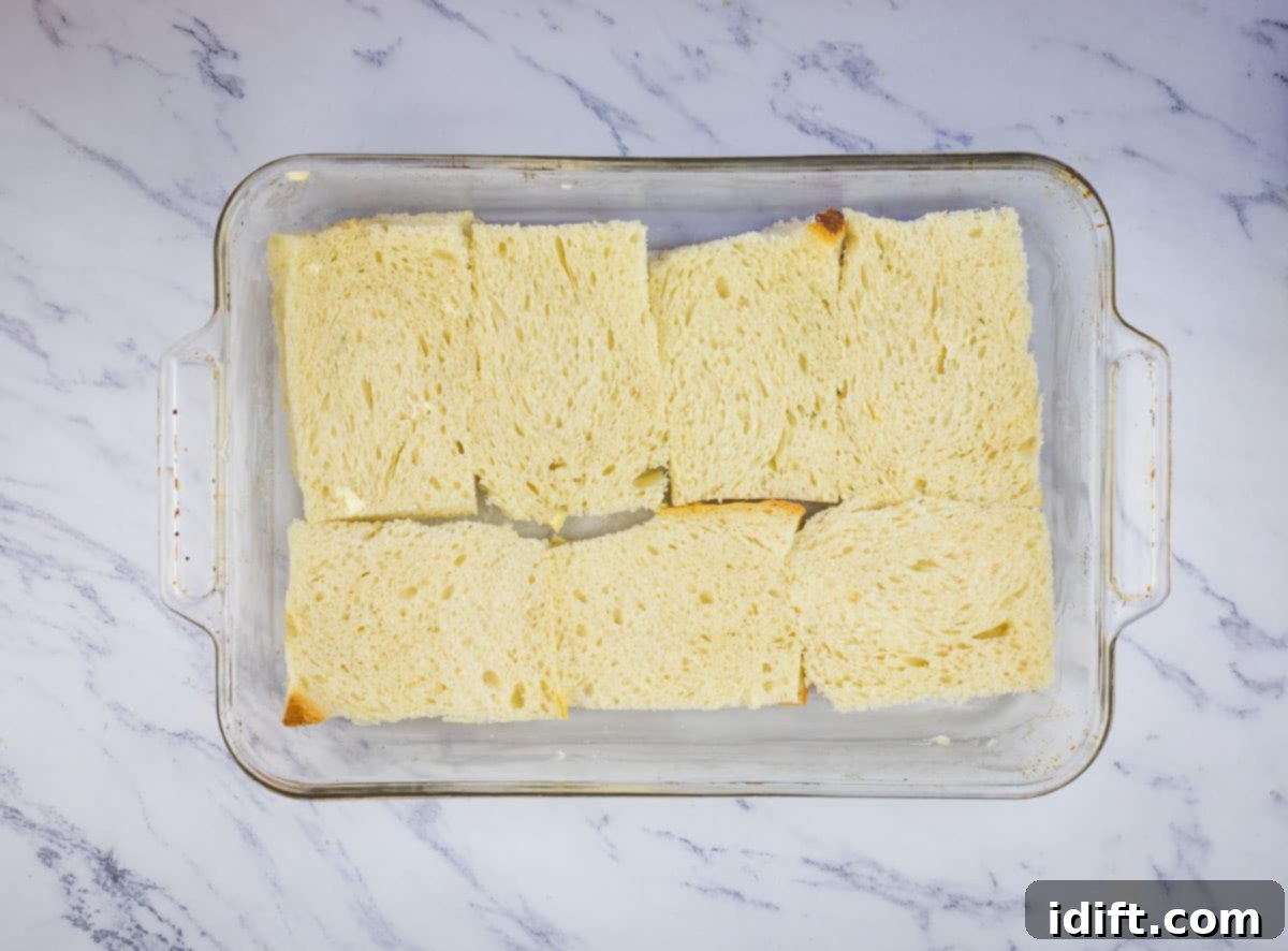 Bread layered neatly in the bottom of a buttered baking dish.