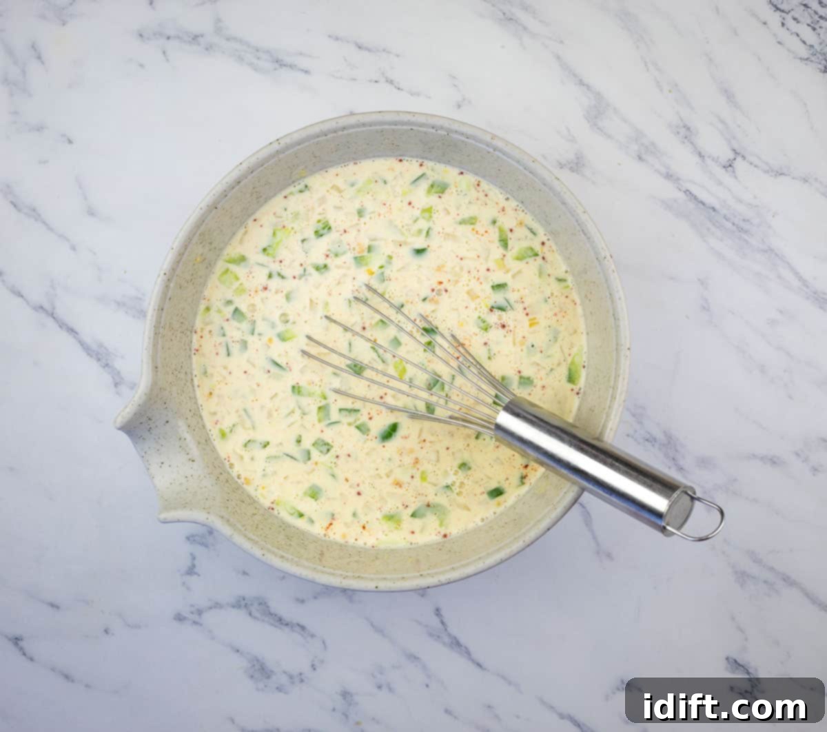 A bowl showing eggs, milk, chopped onion, peppers, and seasonings being whisked.