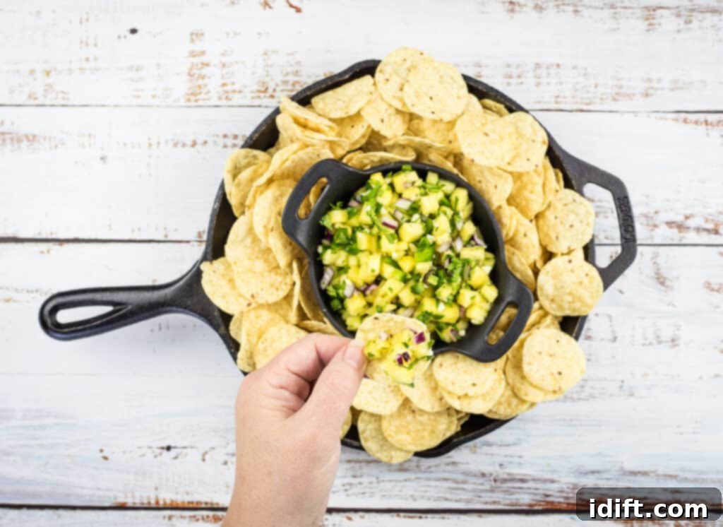 Lone Star Pineapple Salsa 6 A hand holding a tortilla chip generously topped with fresh pineapple salsa, showcasing the vibrant colors and chunky texture.