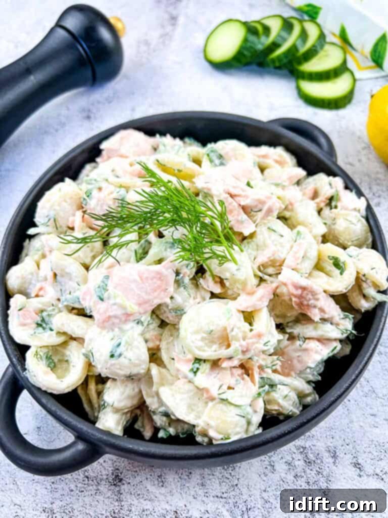 Salmon Pasta Salad in a bowl with lemon and cucumbers in the background.