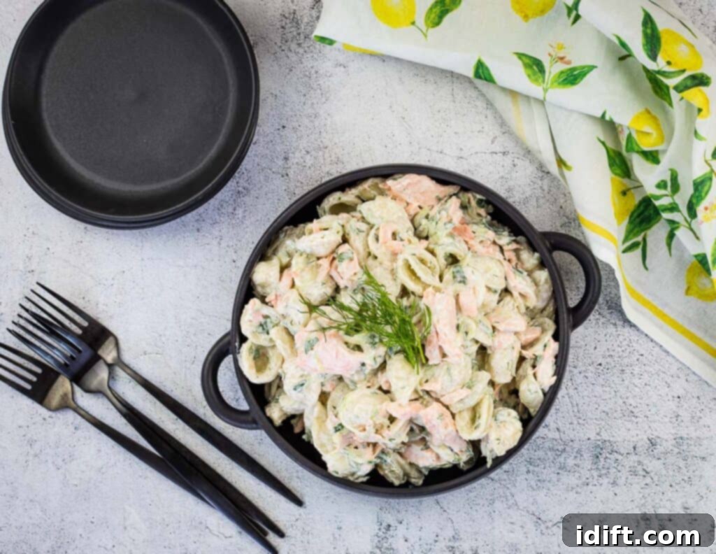 Salmon pasta salad in a black bowl with forks and plates nearby.