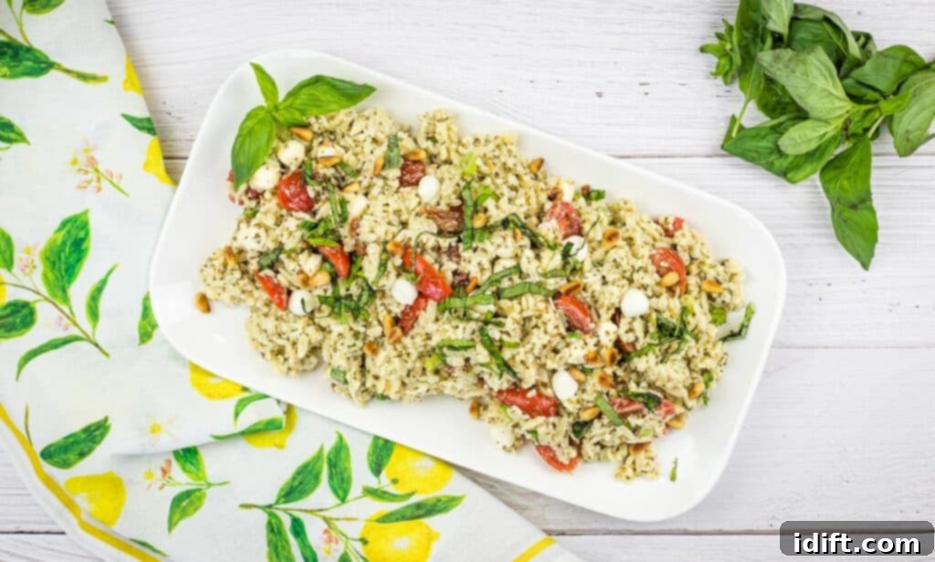 A close-up of Pesto Orzo Salad served on a white plate, highlighting the fresh grape tomatoes and mozzarella pearls.