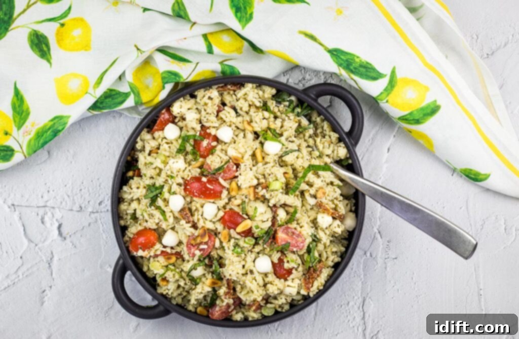 A top-down view of Pesto Orzo Salad generously served in a black bowl, garnished with fresh basil.