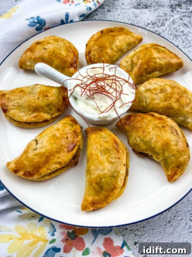 Crispy golden-brown air fryer beef empanadas arranged enticingly on a white plate, garnished with fresh cilantro, ready to be served.