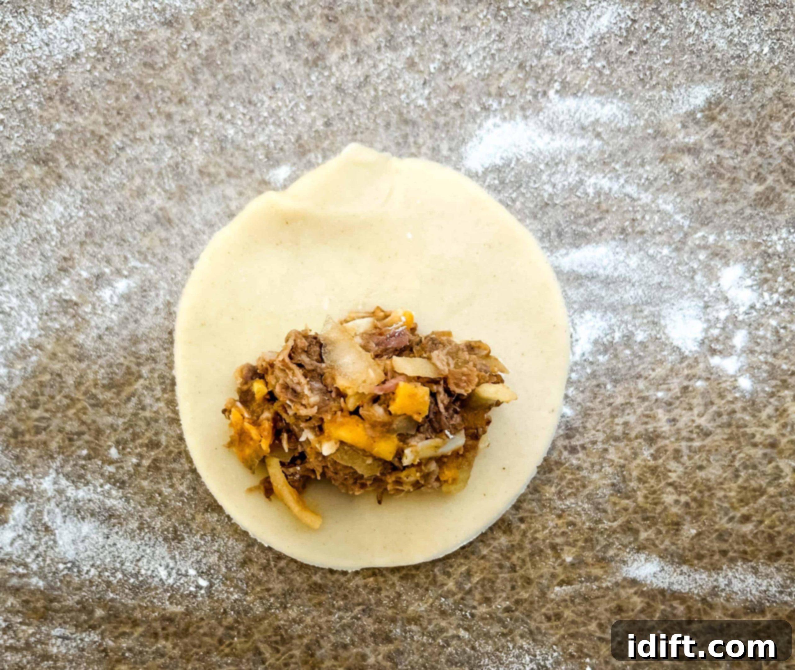 A close-up shot of a pastry disc with a spoonful of beef filling placed on one half, leaving ample space around the edges for sealing.