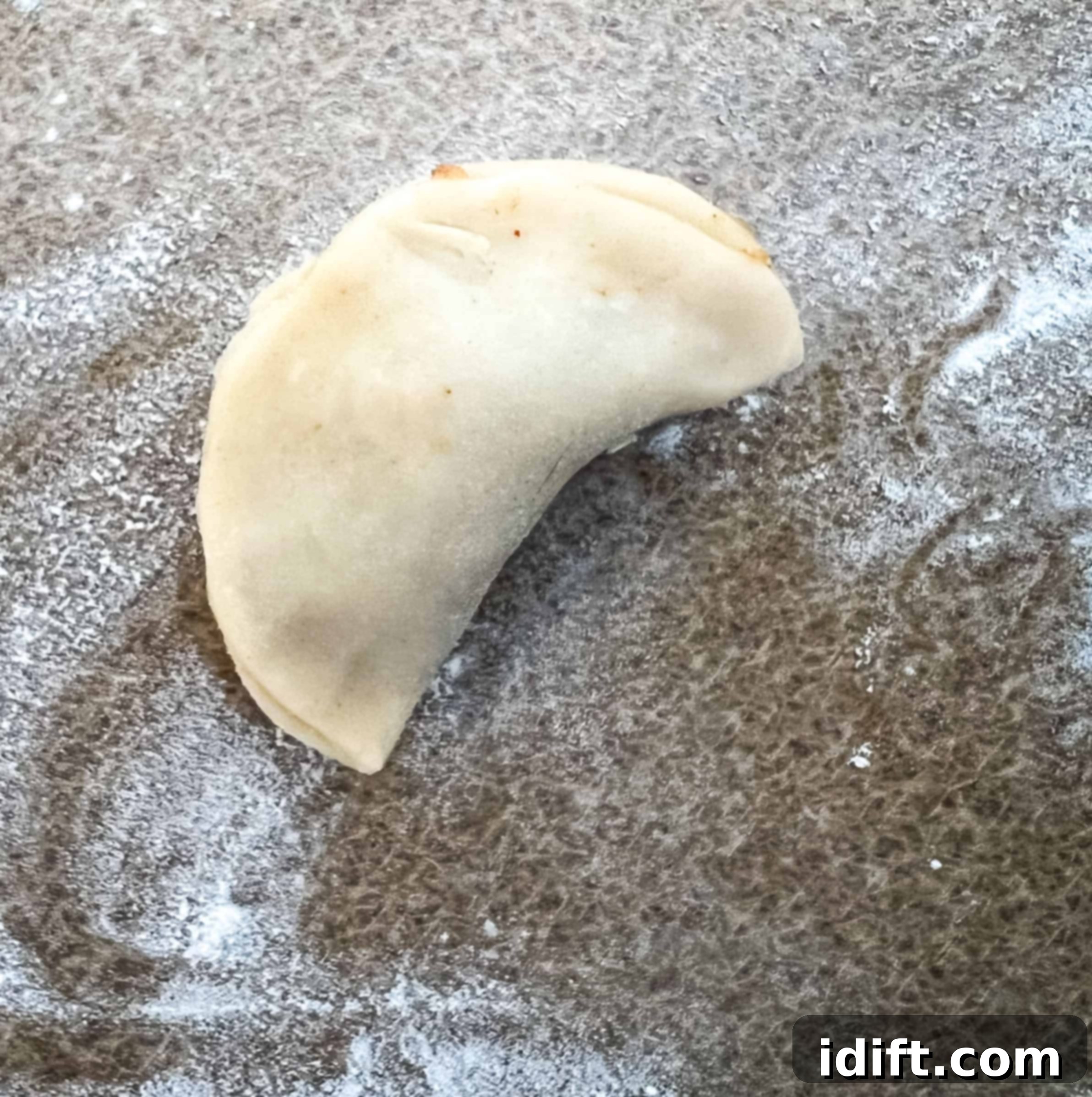 A freshly folded empanada with its edges firmly pinched together, showing a neatly crimped border created by a fork.