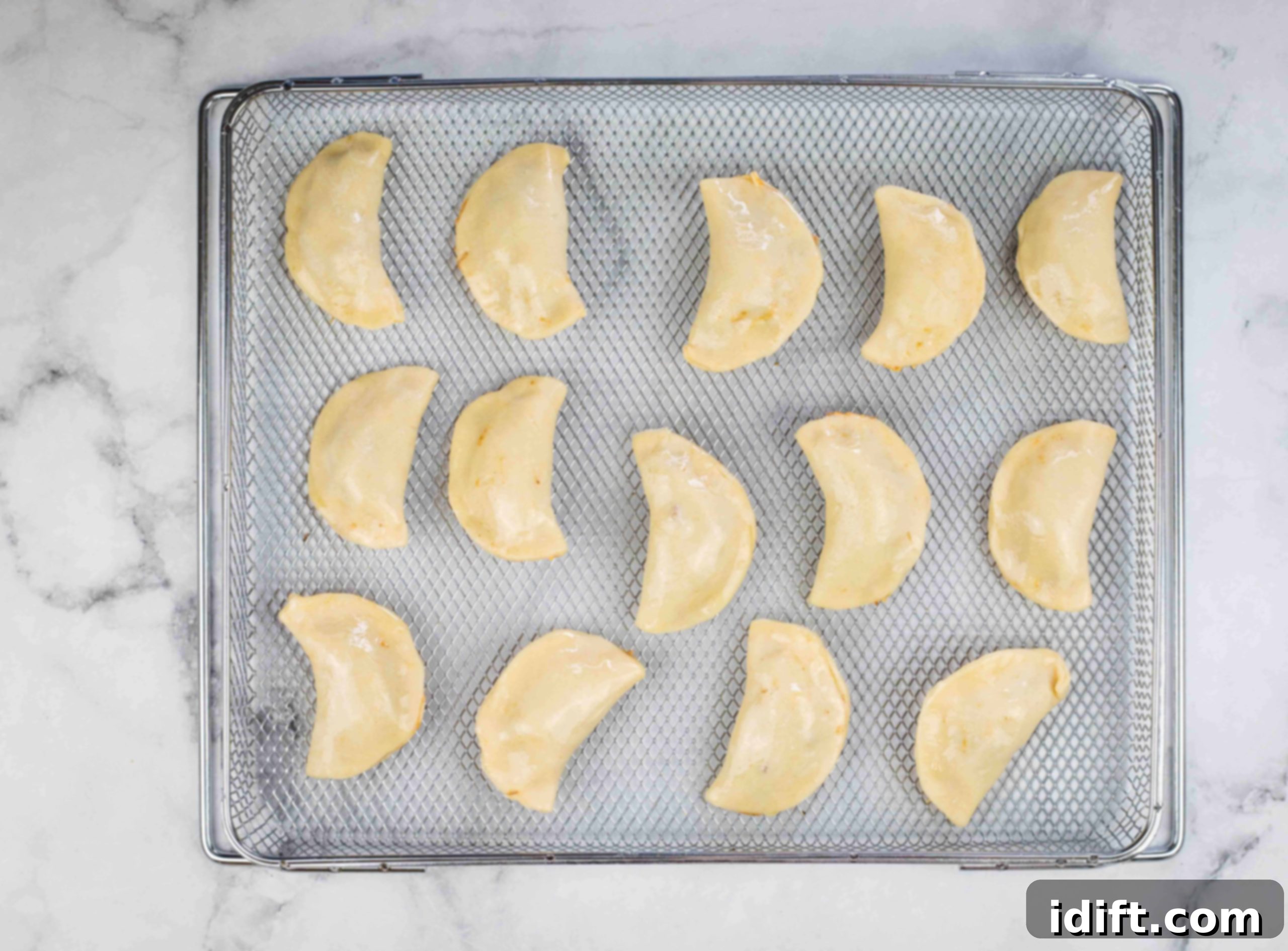 Several raw beef empanadas arranged on an air fryer rack, brushed with egg wash and ready for cooking.