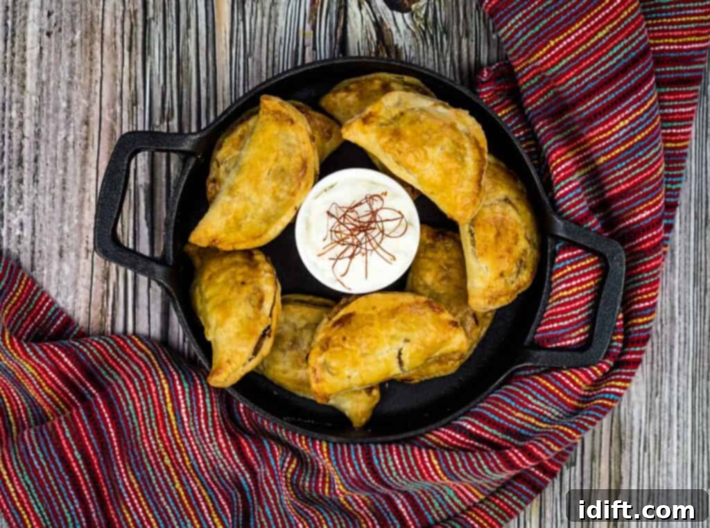 An overhead view showcasing a plate of freshly cooked air fryer beef empanadas, their perfectly browned crusts indicating a delightful crispness, garnished sparingly with herbs.