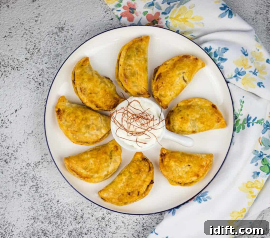 A close-up, top-down view of several golden-brown air fryer beef empanadas on a plate, highlighting their crimped edges and a hint of the savory filling peeking out.