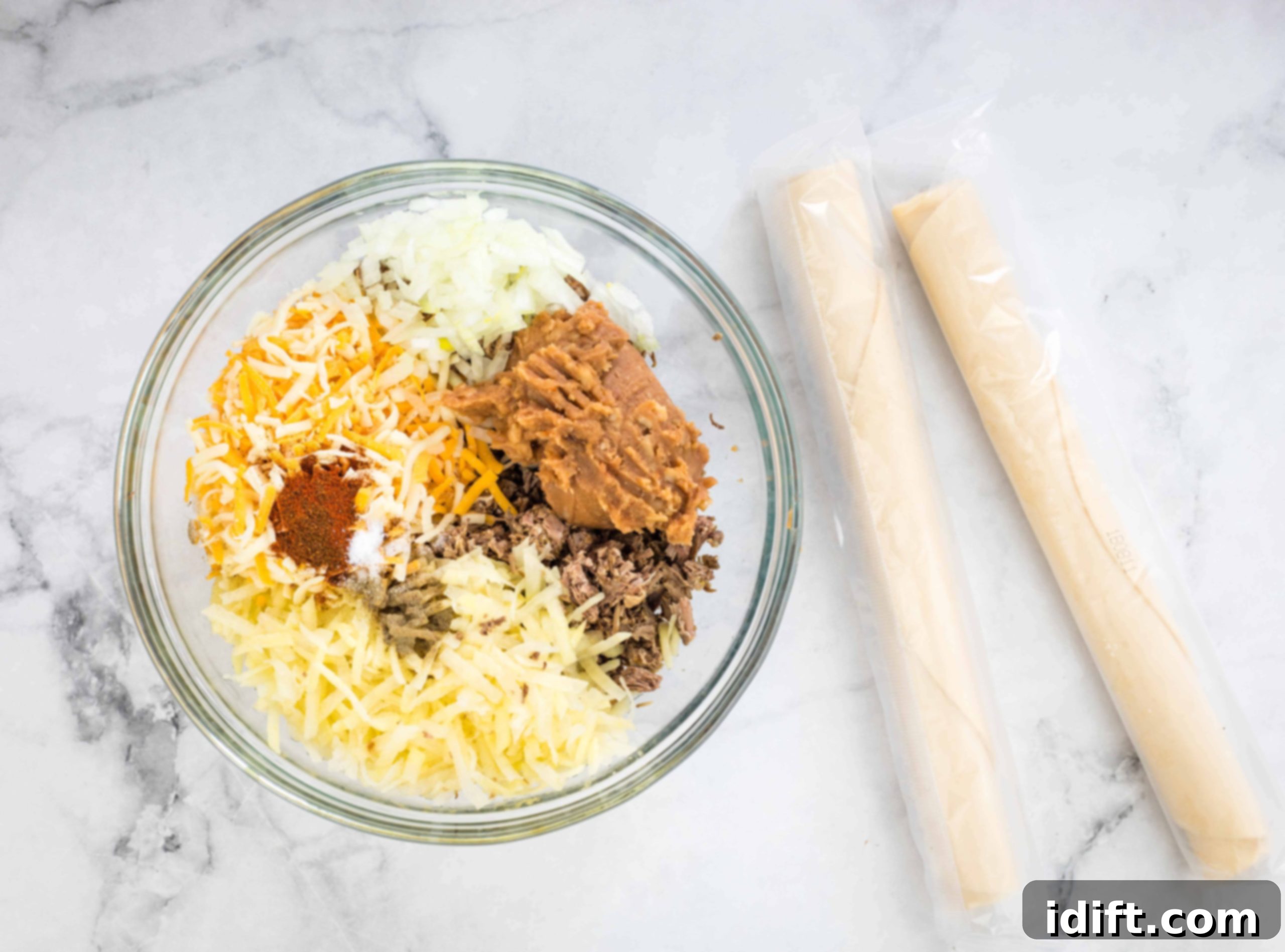A large bowl containing a mix of shredded beef, cheese, potatoes, refried beans, and chopped onions, well combined.