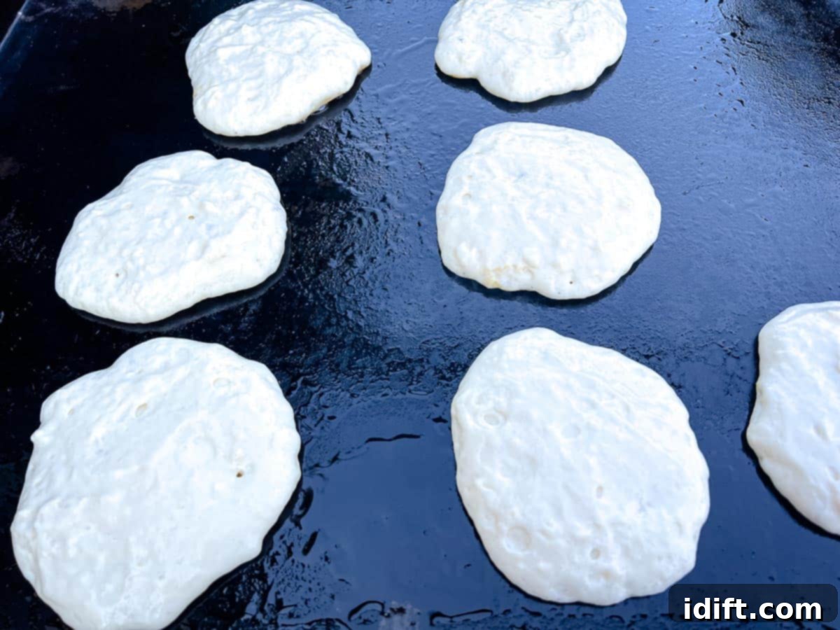 Fluffy pancake batter being poured onto a hot, oiled Blackstone Griddle, forming several round pancakes.