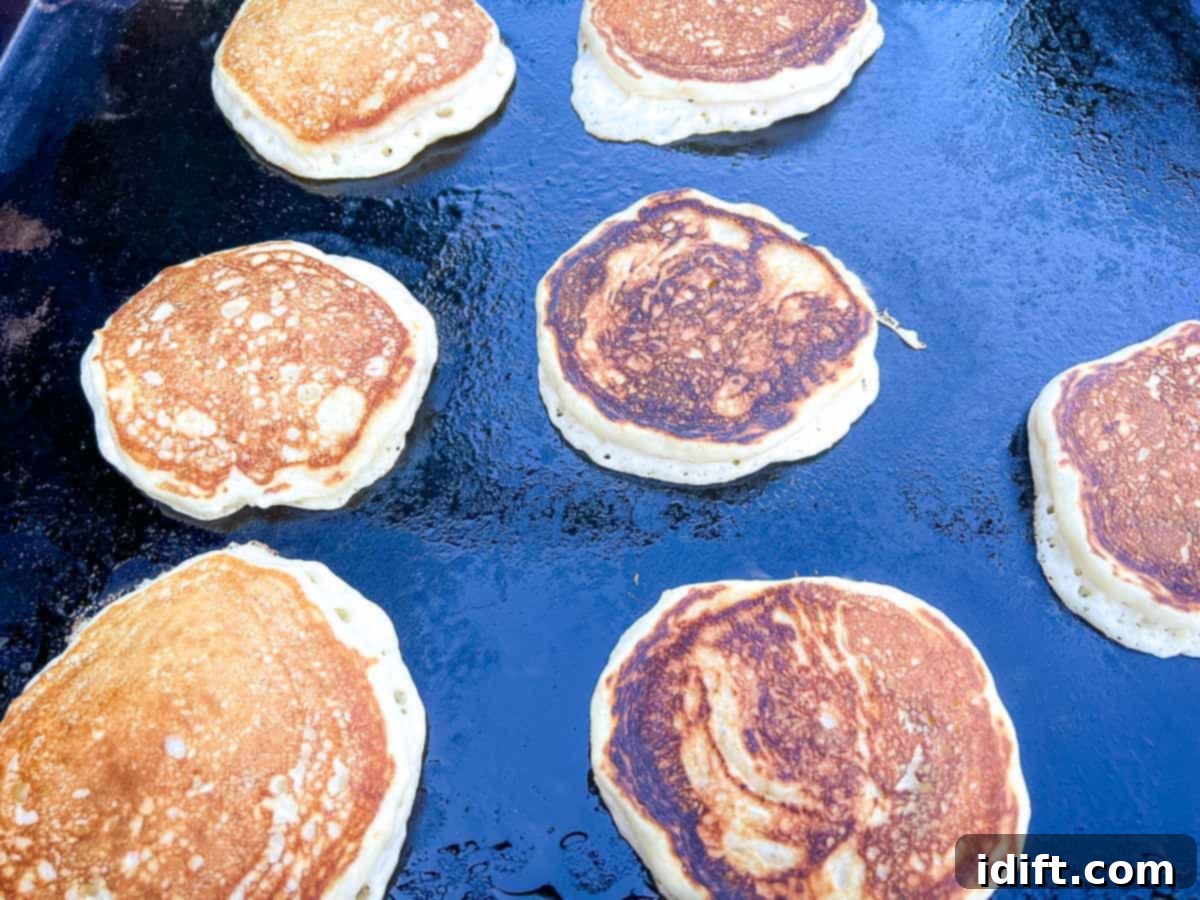 Several pancakes cooking on a Blackstone griddle, showing the golden-brown underside of a recently flipped pancake and bubbles forming on the raw side.