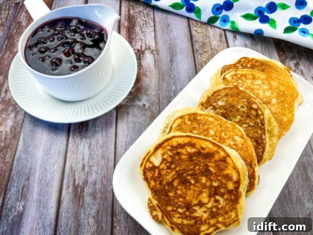 A platter of fluffy buttermilk Blackstone Pancakes, ready to be served, with a bowl of homemade blueberry sauce in the background.