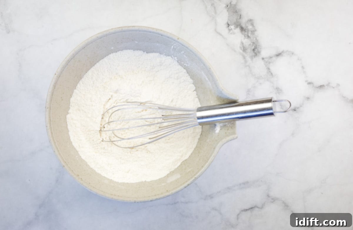 Dry ingredients for pancakes, including flour, sugar, baking powder, baking soda, and salt, mixed together in a large mixing bowl.