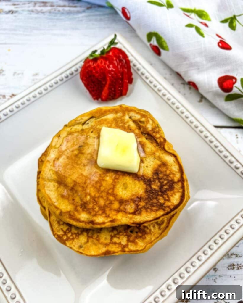 A stack of golden brown Sweet Potato Pancakes generously topped with toasted pecans, served on a rustic plate, with a fresh strawberry and a warm beverage in the softly blurred background, evoking a comforting breakfast scene.