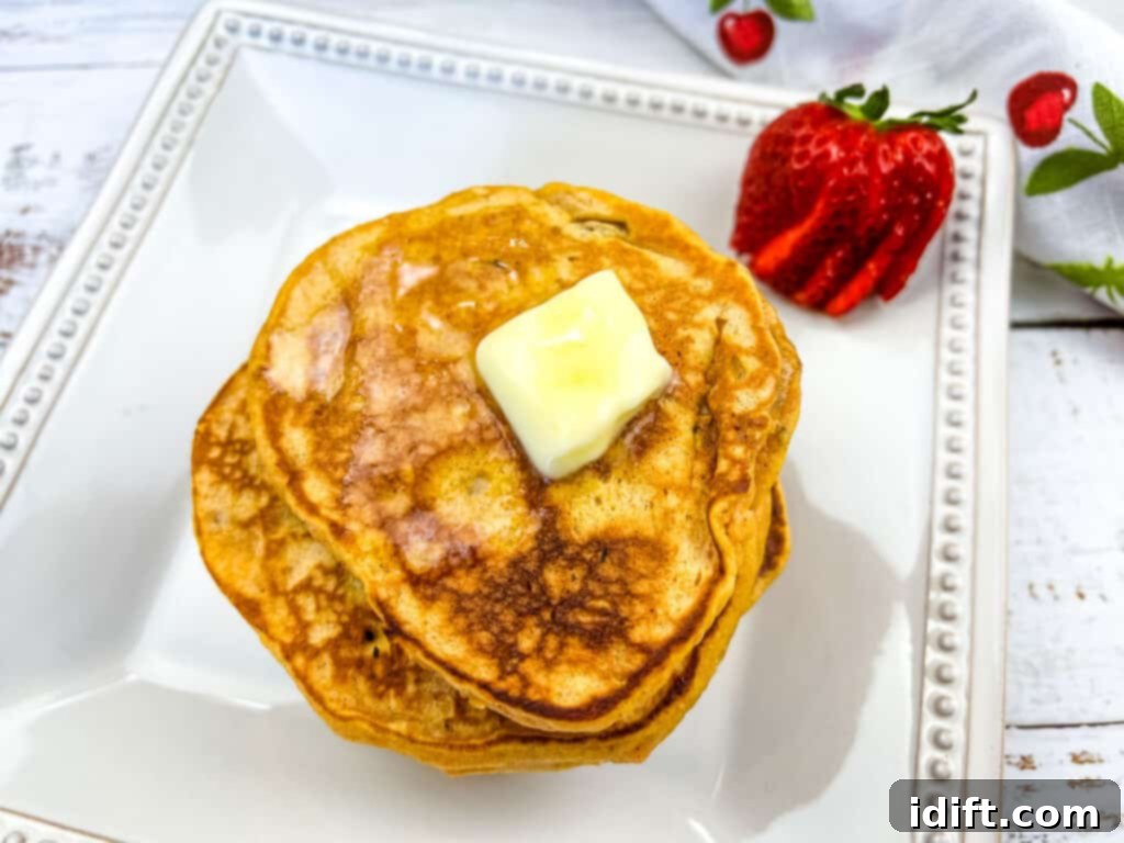 Another perspective of a stack of Sweet Potato Pancakes adorned with chopped pecans, placed on a white plate with a single strawberry as a garnish, ready for a delicious breakfast.