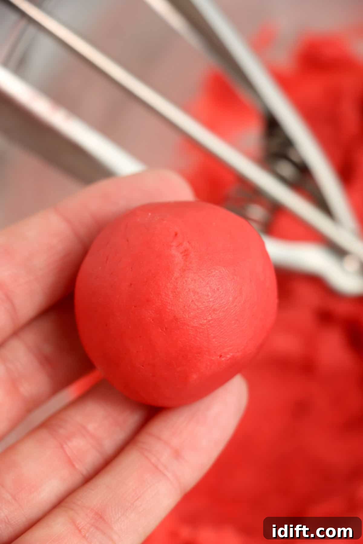 Hands rolling a scooped portion of red velvet truffle dough into a smooth ball.