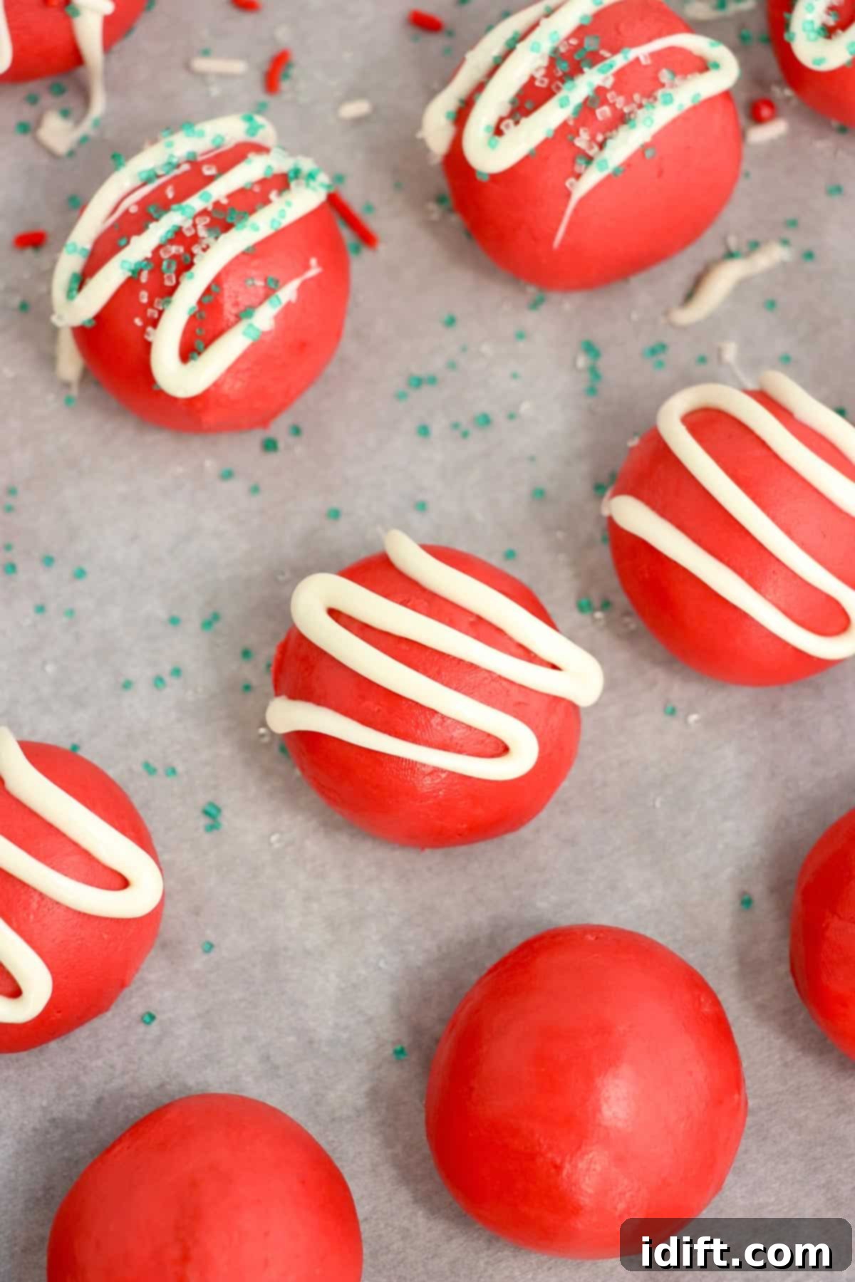 Finished red velvet Christmas truffles, decorated with white chocolate drizzle and sprinkles, arranged on a sheet pan.