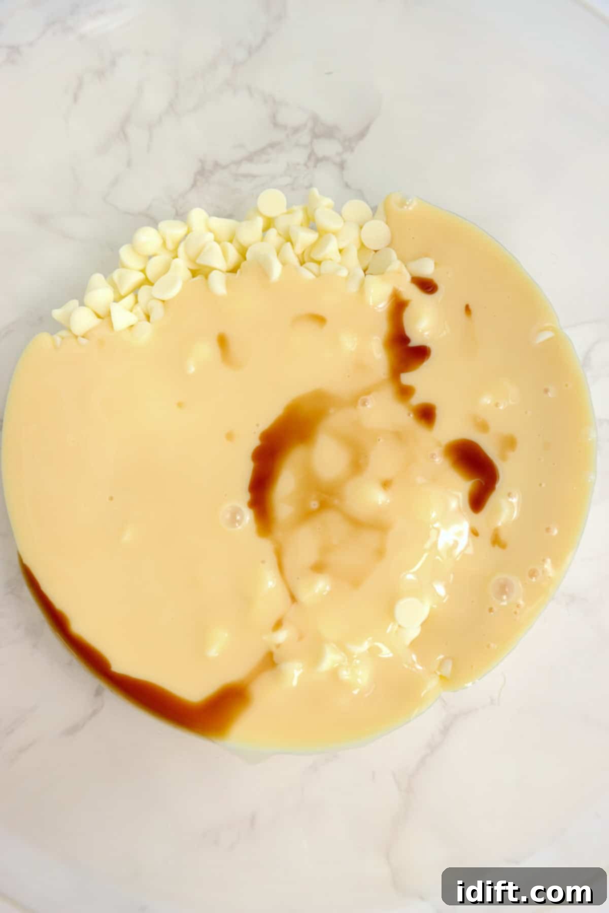 Vanilla being added to white chocolate chips and sweetened condensed milk in a bowl.