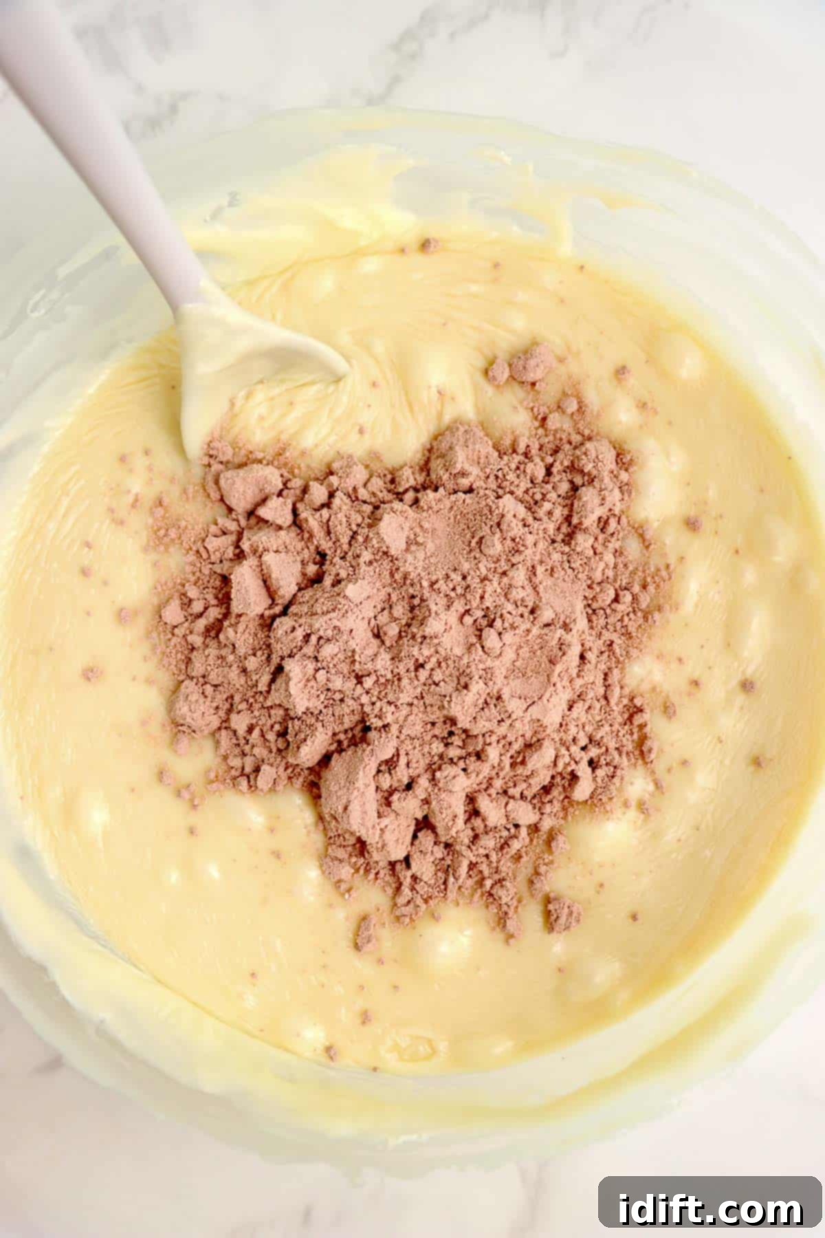 Red velvet cake mix being stirred into the melted chocolate mixture.