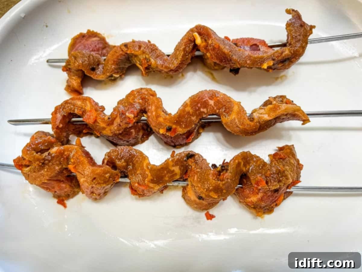 Sizzling Steak Skewers with Zesty Mojo Rojo 9 Marinated steak strips expertly threaded onto several metal skewers, ready for grilling.